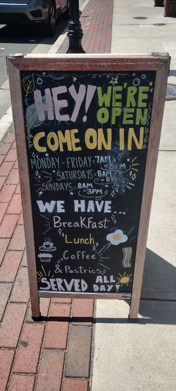 Hand-painted A-frame chalkboard — Hey! We're Open Come On In · Monday-Friday 7am-5pm, Saturdays 8am-5pm, Sundays 8am-3pm · We have Breakfast, Lunch, Coffee &amp; Pastries served all day