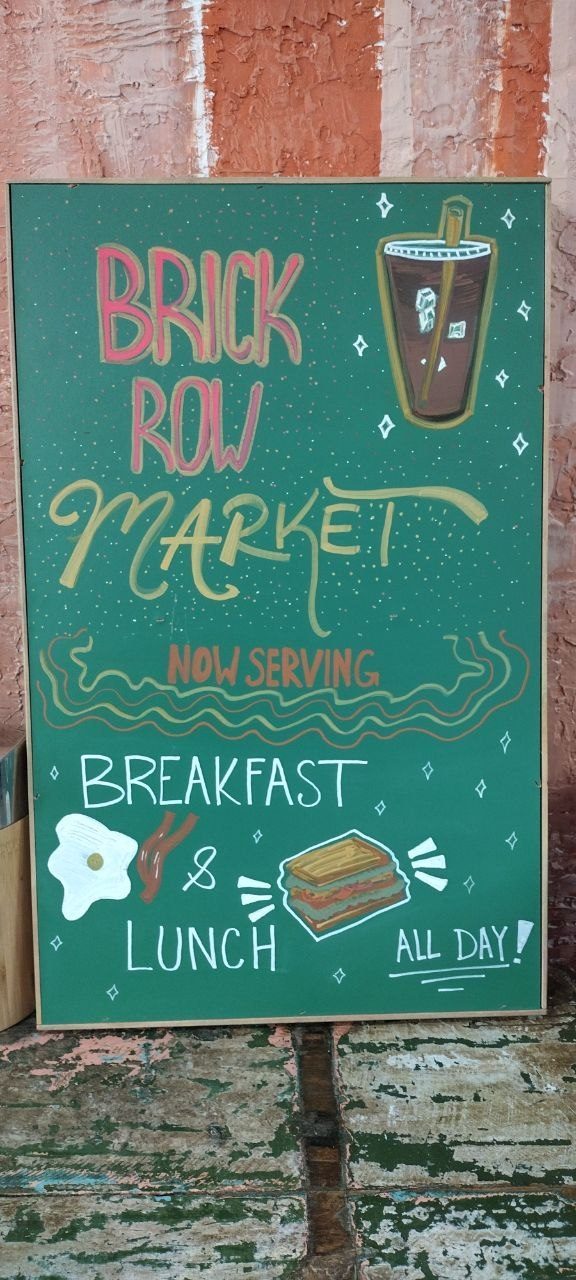 Hand-painted chalkboard sign — Brick Row Market Now Serving Breakfast and Lunch All Day