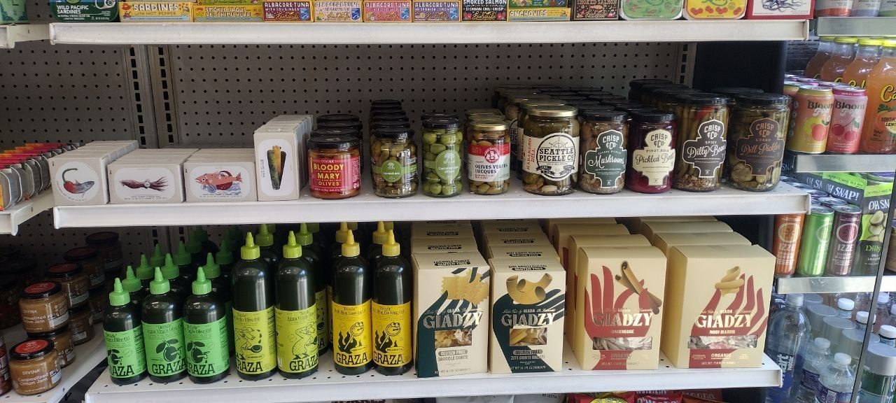 Shelves of Graza olive oil, Giadzy pasta, jarred olives, and gourmet pickles — hard-to-find pantry goods