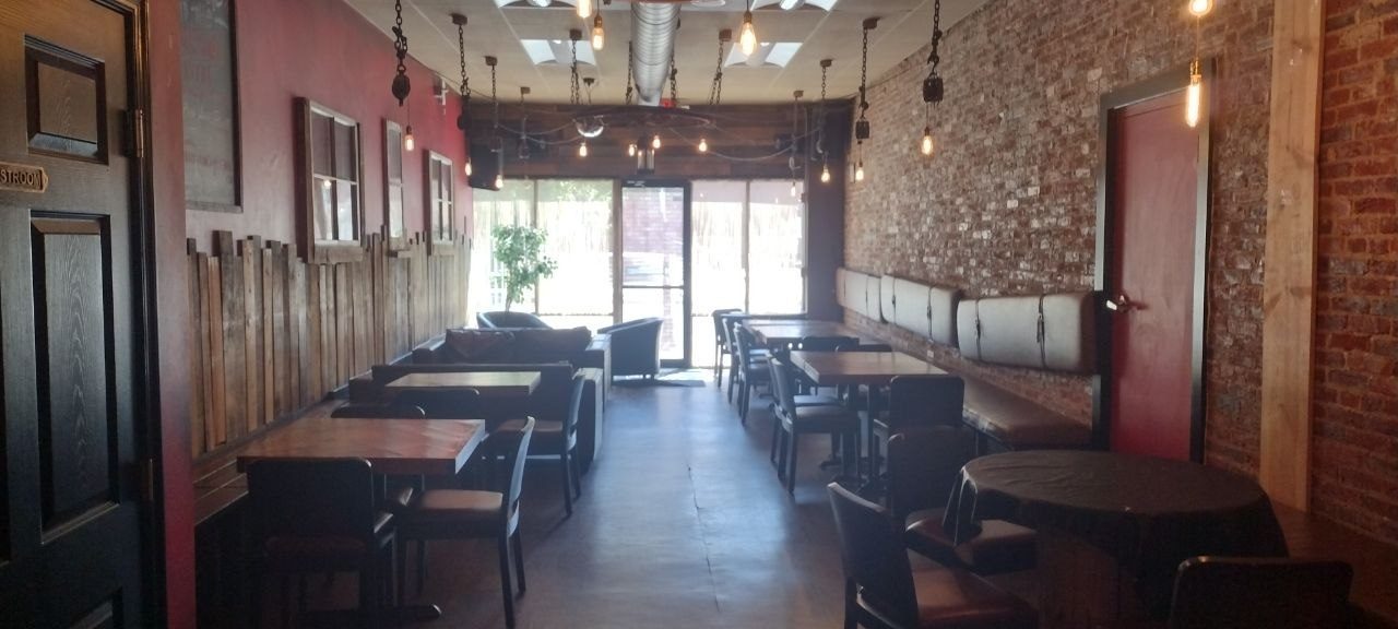 Long view of the dining room with Edison bulb pendants on iron chain, exposed brick on the right, tables and chairs down the center