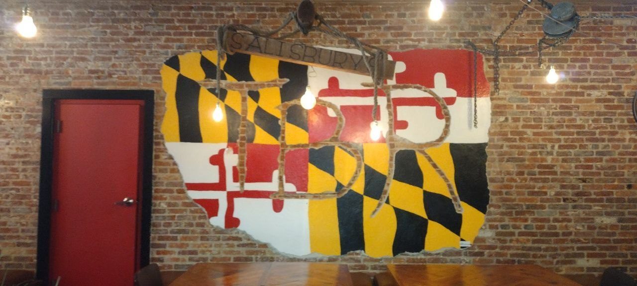 The Maryland flag mural with BR insignia, hanging over a brick wall and Edison bulbs