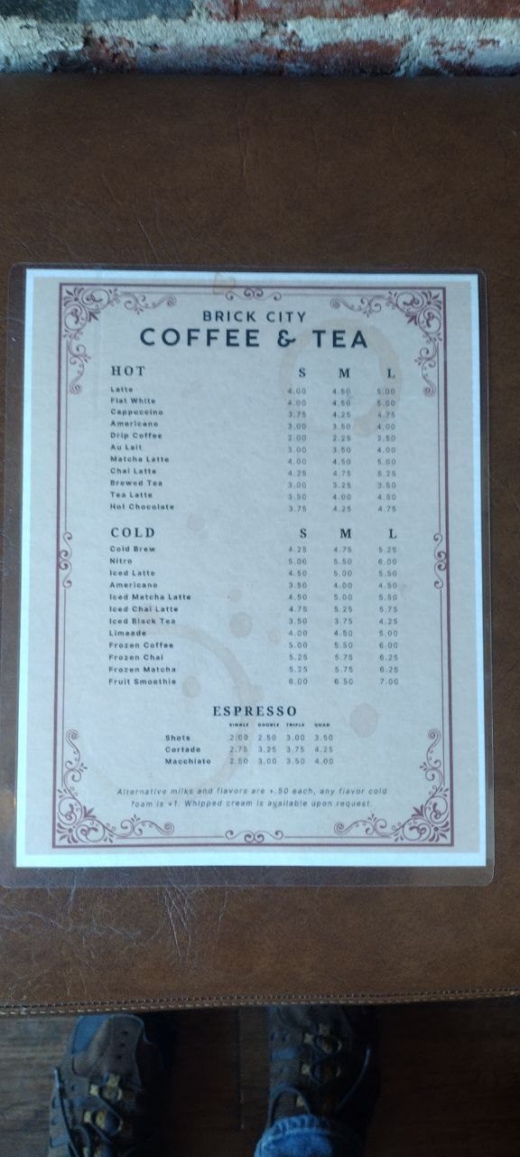 Brick City Coffee &amp; Tea menu on a wooden table — Hot, Cold, and Espresso pricing with small, medium, and large columns