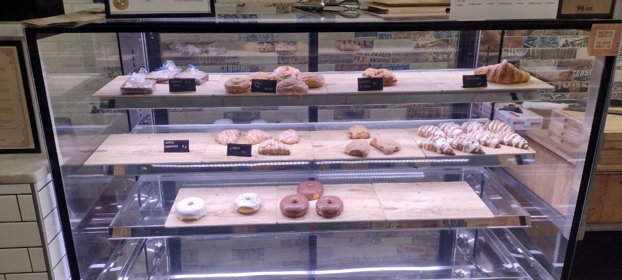 Glass pastry case with three shelves of fresh-baked goods — banana bread up top, croissants and scones in the middle, glazed donuts on the bottom
